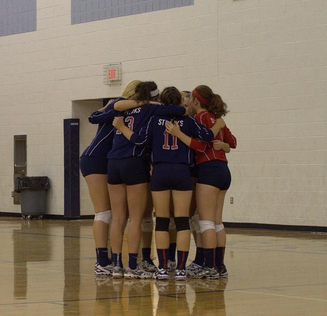 Girls Varsity volleyball team huddles together to discuss strategy.