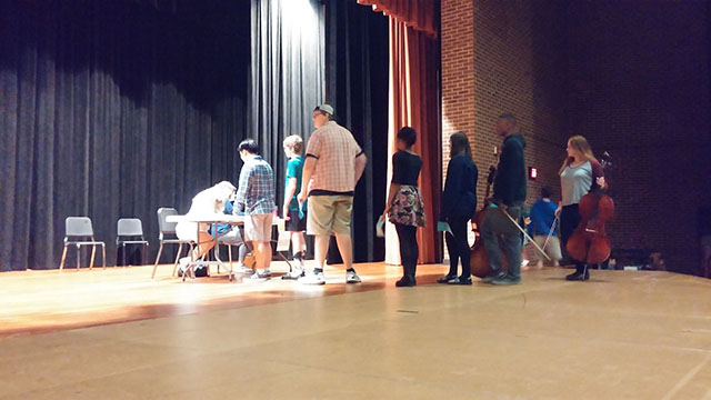 Cellists, violists and bass players wait in line to receive their audition ticket from parent volunteers. They then waited for their number to be called and their audition to begin.