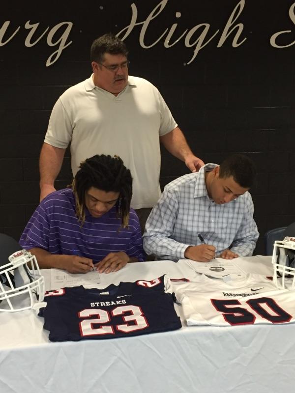 Coach Thurman stands over the boys signing. 