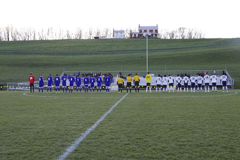 Harrisonburg and Fort Defiance mens varsity soccer teams line up for the playing of the National Anthem.