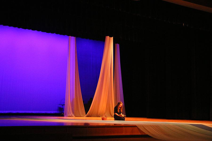 Senior Eleanor Alger sits on stage as her character, Lydia, and reads. 