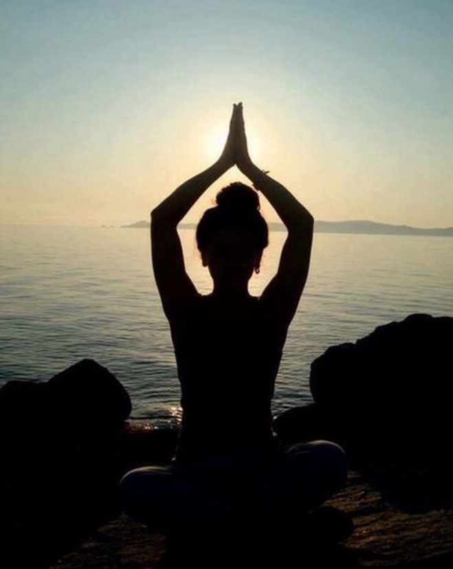 A person practices mediation with a yoga pose, practicing two forms of yoga, by the ocean.  