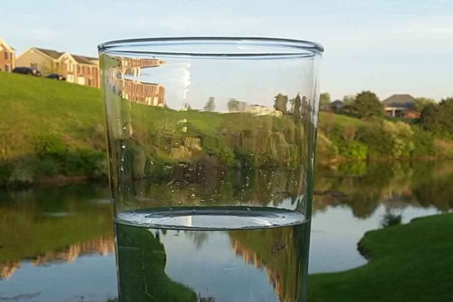 A glass of water sits near a body of water.