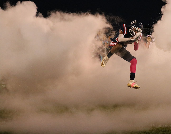 Junior #25 Marquez Sly jumps through the wall of smoke while entering the field before the game.
