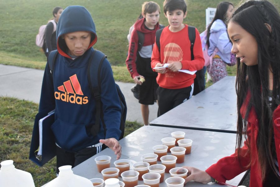 Students grab a small cup of apple cider from the table stationed outside of the track. 
