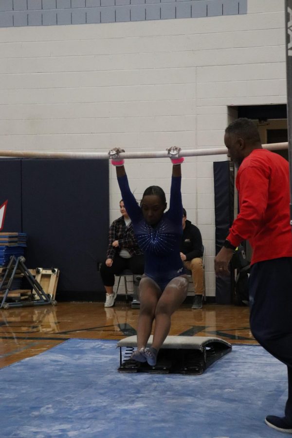 Junior Dorothy Yates mounts the low bar with assistance from coach Michael King by doing a kip to start her bars routine.
