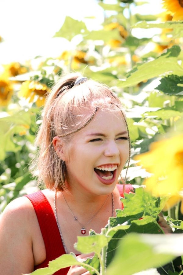 Junior Maren Mcgehee laughs as she poses for a photo in a sunflower field. 