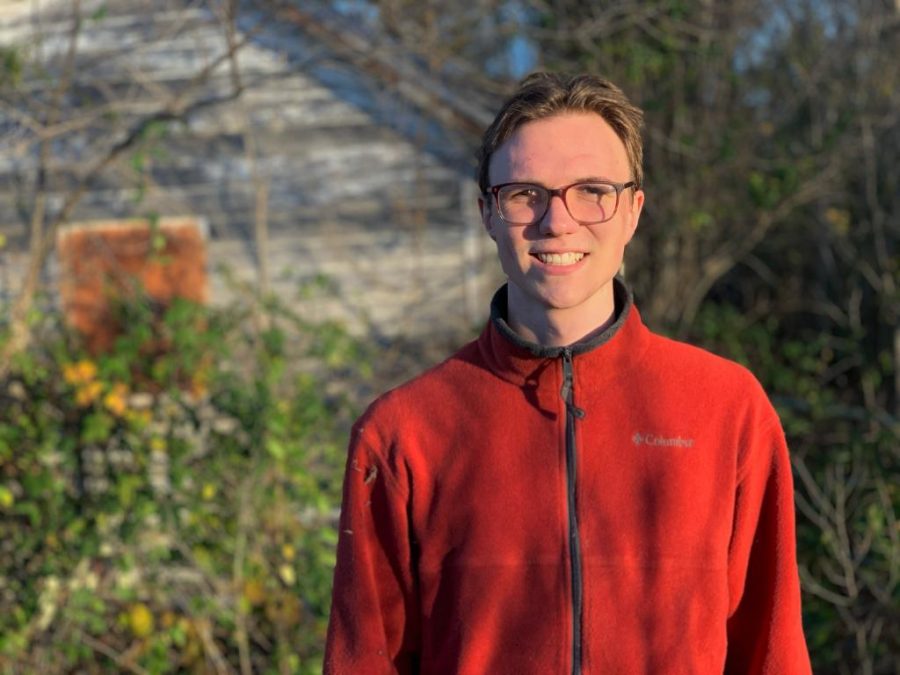 Benevento-Zahner poses in a red fleece Columbia jacket in front of some greenery. He is passionate about the environment. 