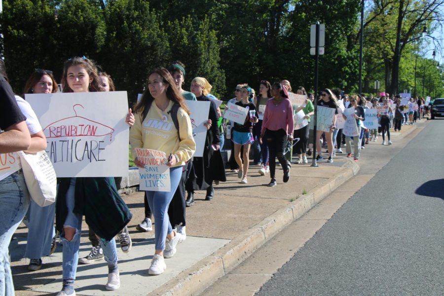 A long line of protesters holding posters while walking to City Hall. 