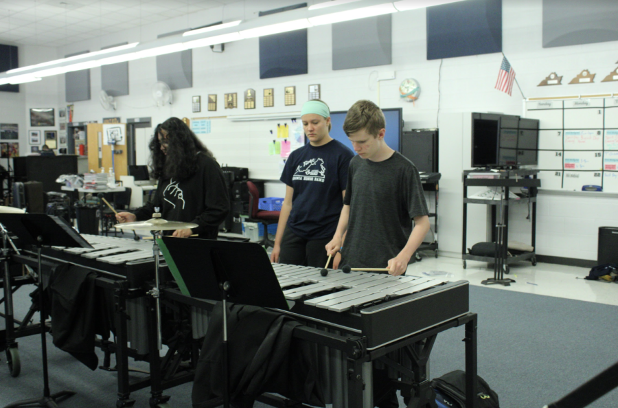These students were practicing inside the band room while the rest of the band was practicing outside. A older student mentors the younger student on the piece of music. 
