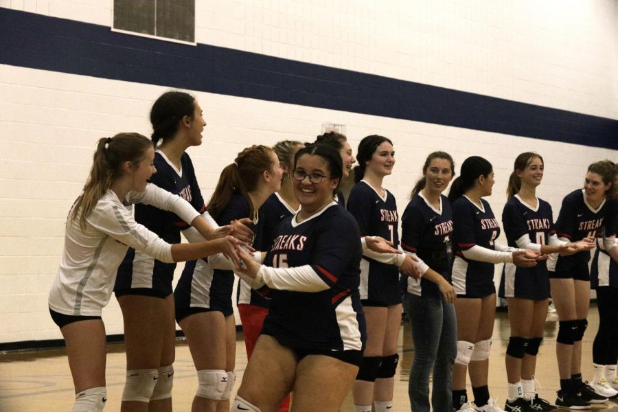 Volleyball team members cheer and give junior Logan Whiting high fives before the game. 