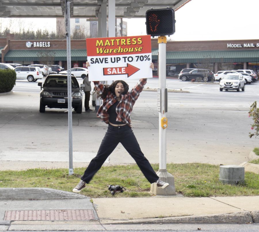 Freshman Jireh Perez jumps with joy as she holds up a sign pointing towards Mattress Warehouse. 