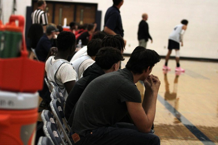 Varsity basketball team watches teammates while playing defense.