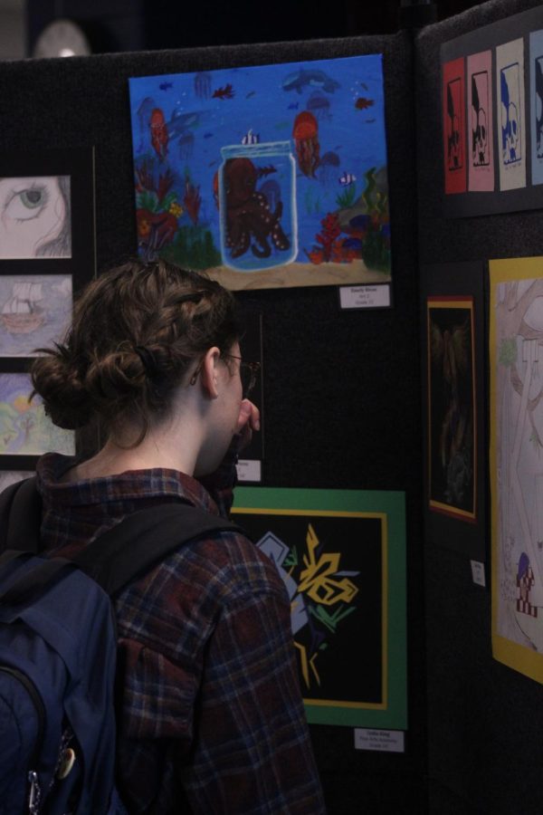 Sophomore Lydia King looks at her artworks showcased outside of the auditorium while the showcase was being set up. King is a part of the cast of "Newsies". 