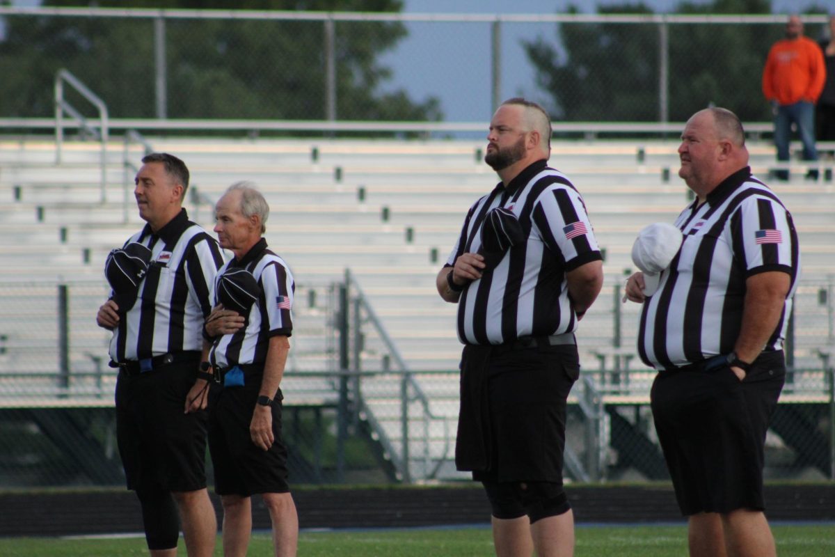 Refs stand and remove their hats for the national anthem before kickoff. 