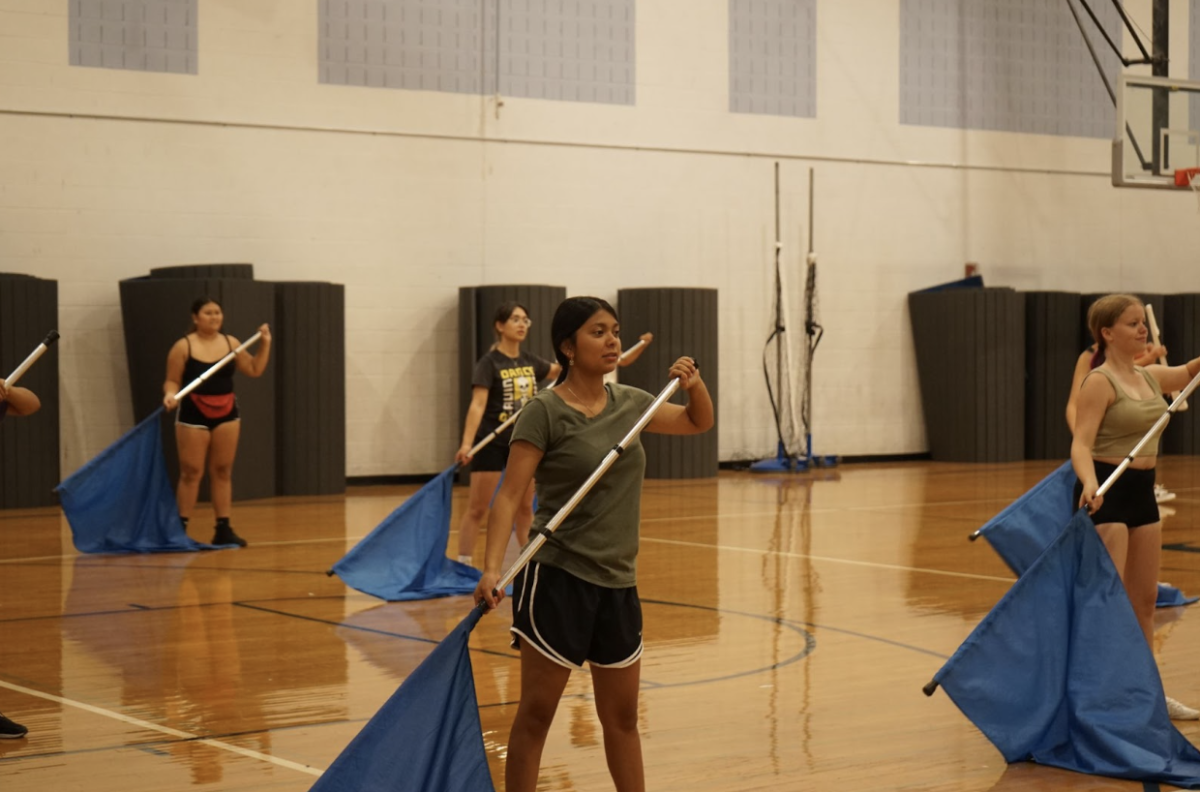Color guard members practice with their flags in the gym.