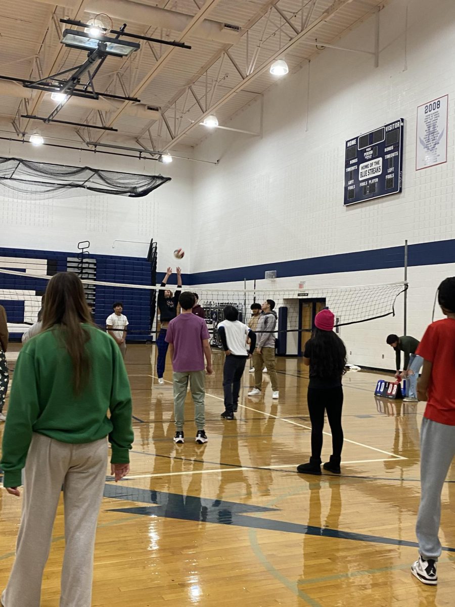 A student hits the volleyball over the net during their game in gym class.