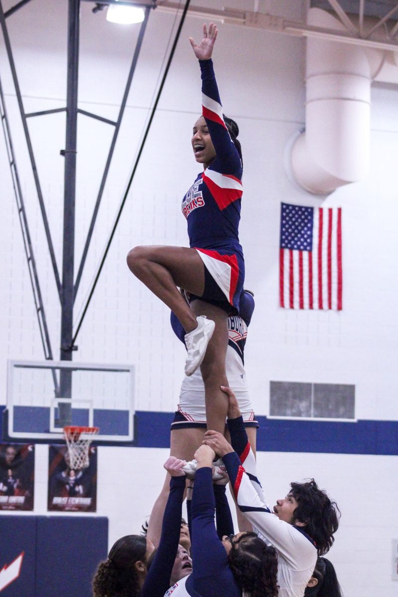 Junior Varsity Cheerleader waves to crowd as she does a stunt. 