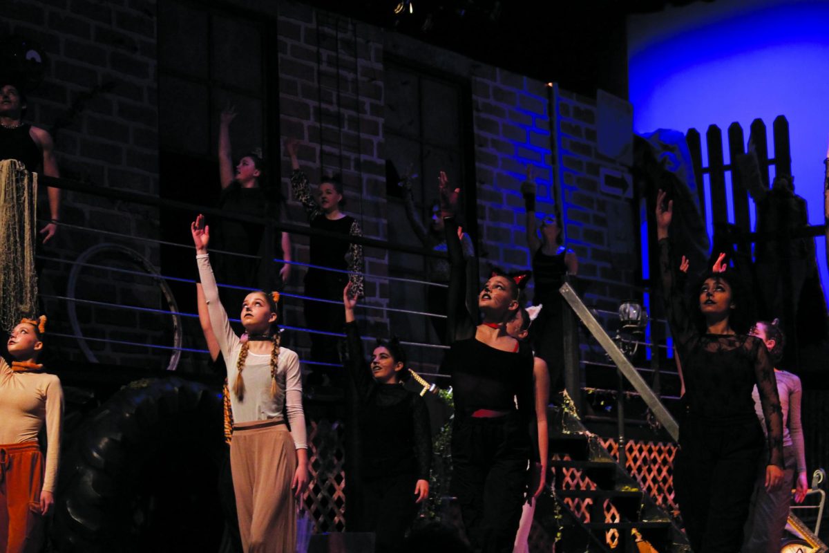 Cats ensemble cat, Demeter, and Coricopat, played by Molly Wells, Sophia Pimentel Yoder, and Ayiana Thornton finish their performance with their hands to the air. 