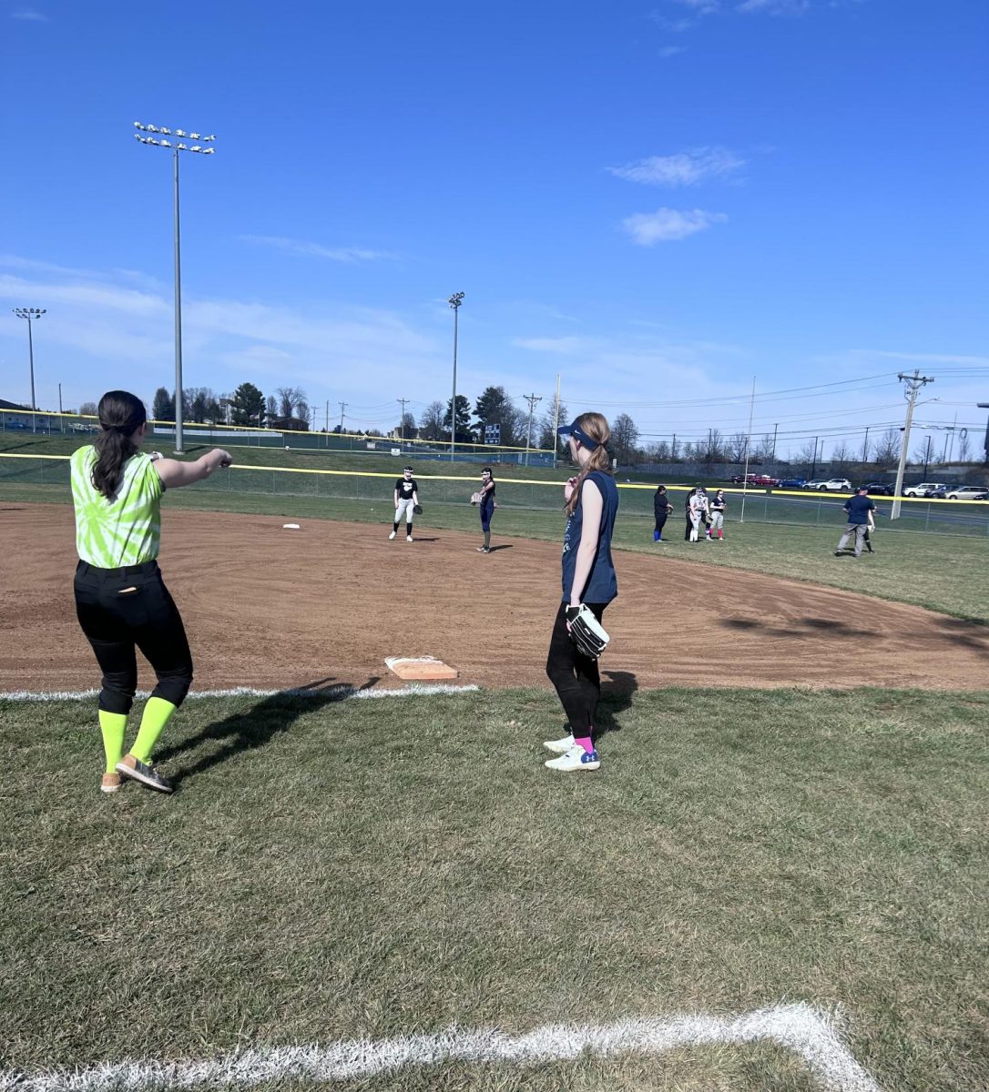 Senior Rylee Stroop assists 8th grader Bella Jones with making a play at 1st base.