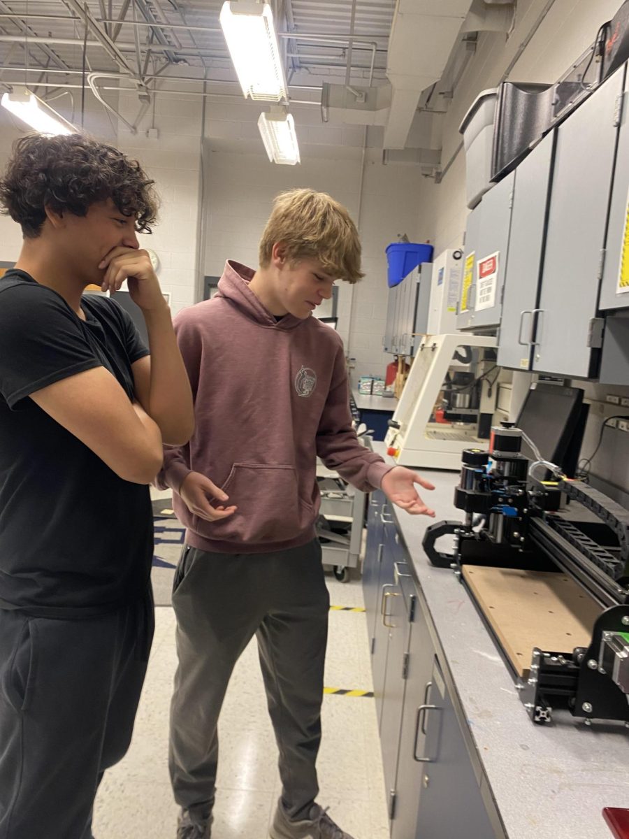 Otis Bawcombe explains to other student about the machine he's using