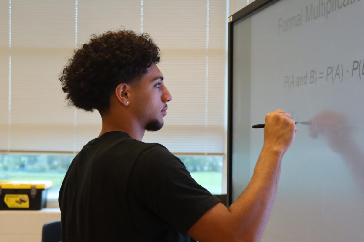  Senior Filipo Toelau writes the formula on the board for his DE Statistics class. “My favorite class this year is probably DE Statistics because the class is challenging and it makes me actually work hard to complete assignments.” Toelau said.
