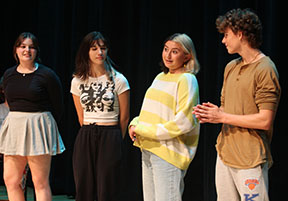 Performers talk to the audience, explaining an improv game that they will play.