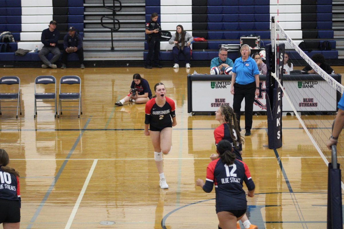 As the Harrisonburg High School Varsity Volleyball team starts a match, Nora Von Rotz spikes the ball and thrives to give the team a point. Rotz celebrates by heading towards her teammates and shouting with pride.