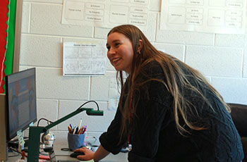 French teacher standing beside her desk laughing with a student