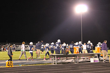 Football players walking to the right side of the field.