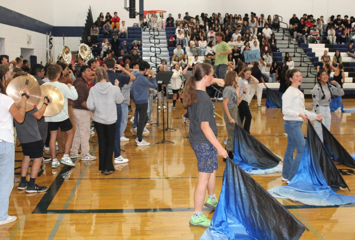 In this picture it shows that both the band and color guards were performing together at the Pep Rally surfaced at Harrisonburg High School. The color guards used the beats and measures from the band music to add onto their performance, they were all in sync and it was truly amazing to watch.