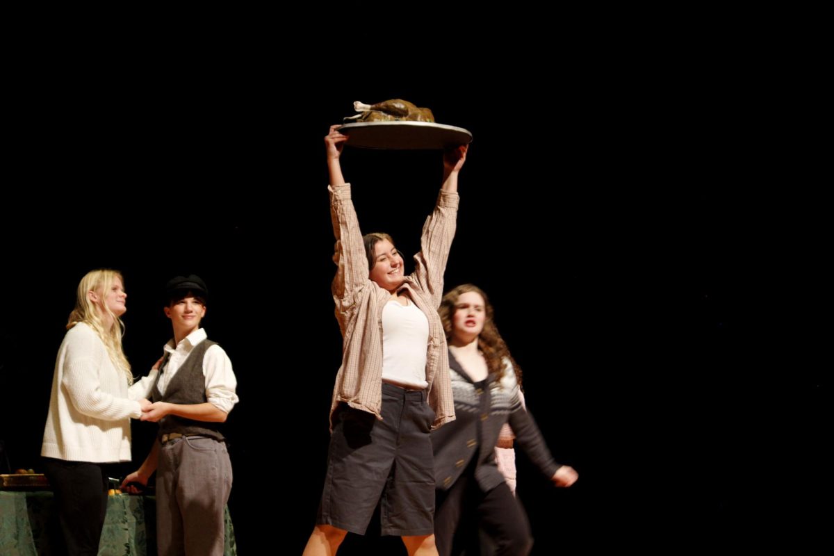 A young Cratchit (Abby Bloss), lifts a turkey above her head in triumph.