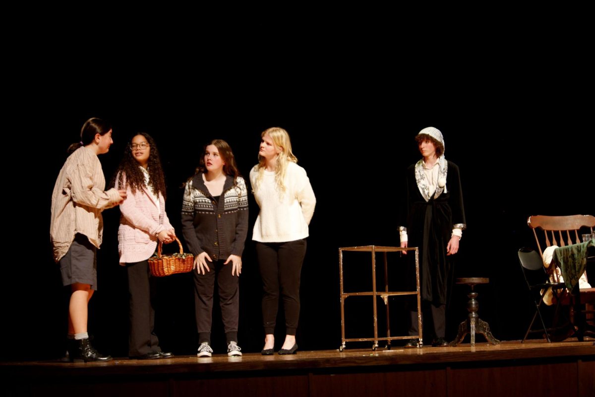 Scrooge (Ell Norment) looks on as Bob Cratchit (Lila Hostetler) and his family prepare for a joyful Christmas meal.