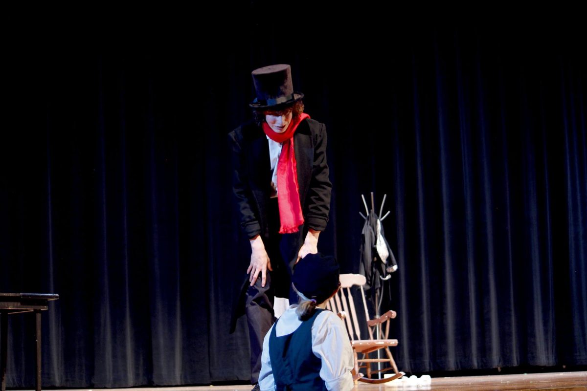 Scrooge (Ell Norment) after a change of heart, asks a young boy (Abby Bloss) to buy the prized turkey from a store.