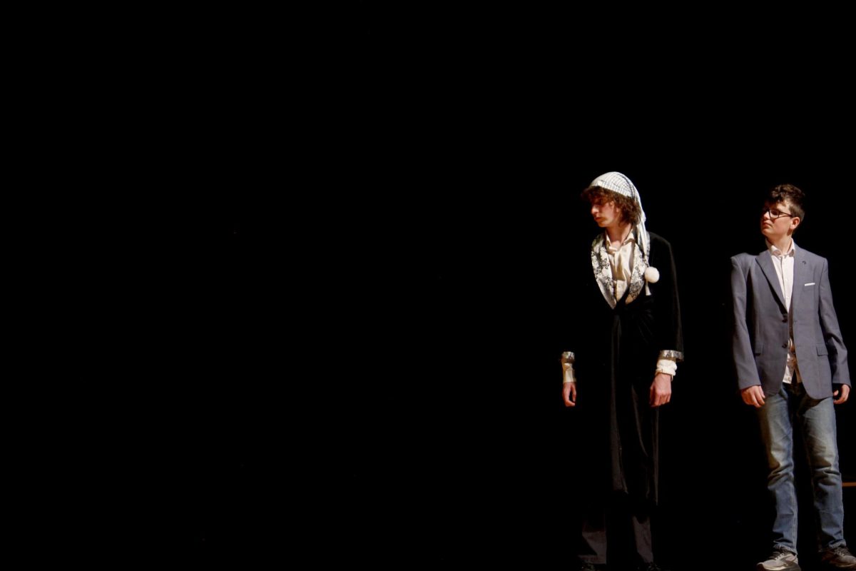 Scrooge (Ell Norment) and The Ghost Of Christmas Present (Shea Gibson) look on as the Cratchit's Christmas meal begins.