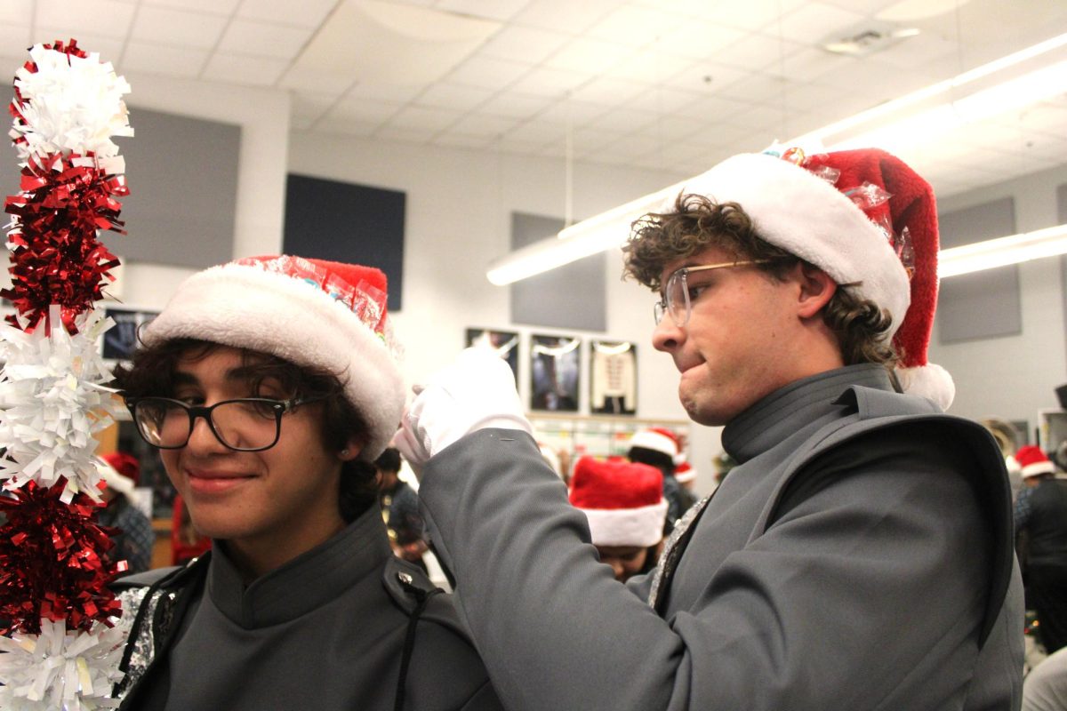 Drum major senior Davis bert puts candy canes in Rocha Salva's santa hat to give out to crowd.