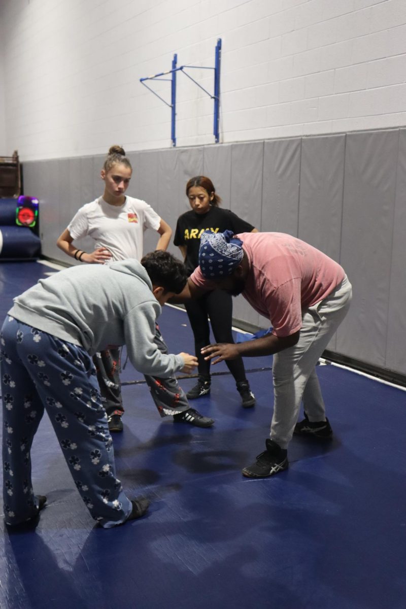 Lucy Hunter and Elana Vargas observing the coach and a teammate demonstrate a move. 