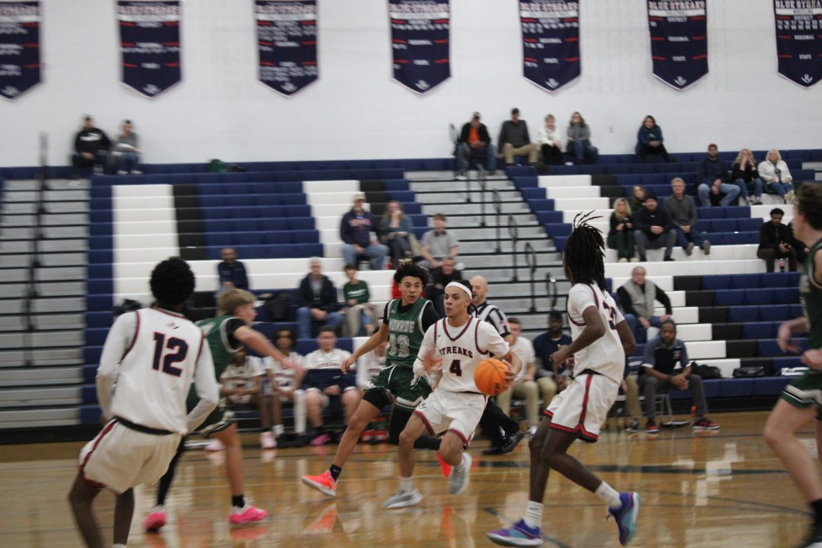 Lazaro Valdivia Arrillaga dribbles the ball in his hand and attempts to avoid the other players from the other school. Valdivia jukes the other team to try and make a shot.
