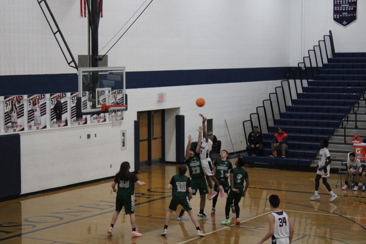 The Harrisonburg High School and William Monroe High school basketball team go head to head and aggressively compete against each other. Pierre Ngeleka jumps as high as he can to try and shoot the basketball into the hoop.
