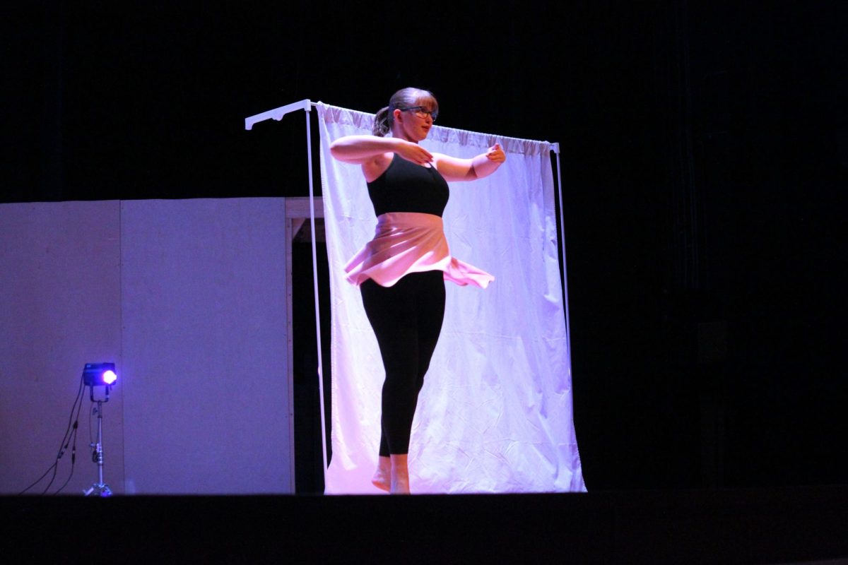 a girl in a black top, black leggings, and pink skirt spins in front a white screen with her arms in front of her