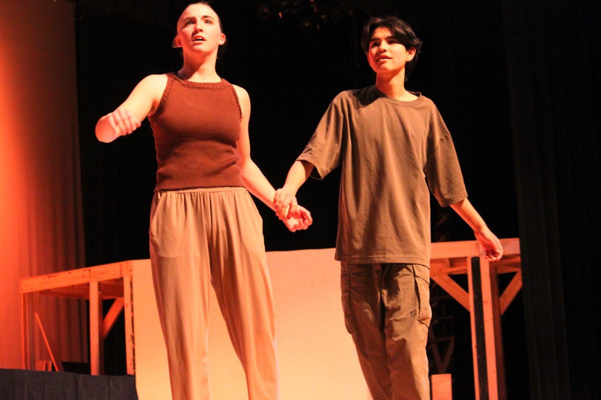 A girl holds hands with a boy while they look to the side
