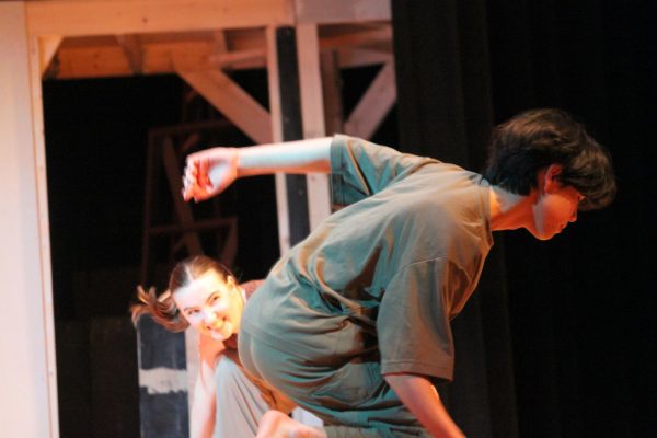 A boy kneels down with one arm extended backwards while a girl farther behind him smiles