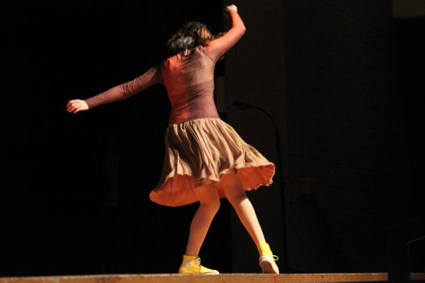 A girl faces away from the camera with arms extended, moving her legs as she dances
