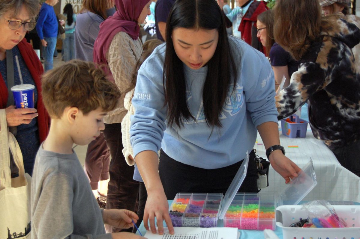 STEM adult helps with necklace booth.