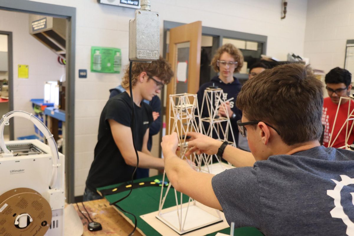 Sophomore Josiah Nafziger leans over the table to put weights on his team's tower.