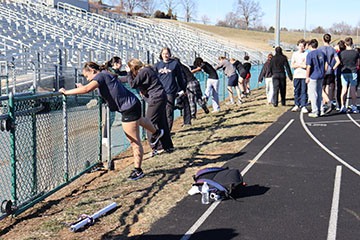 The track team keeping there legs warm by stretching so they don't tense.