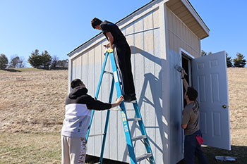Sophomore Josiah Nafziger paints a shed while Freshman Omar Rodriguez holds the latter. " I'm just waiting for my turn to paint," said Rodriguez.