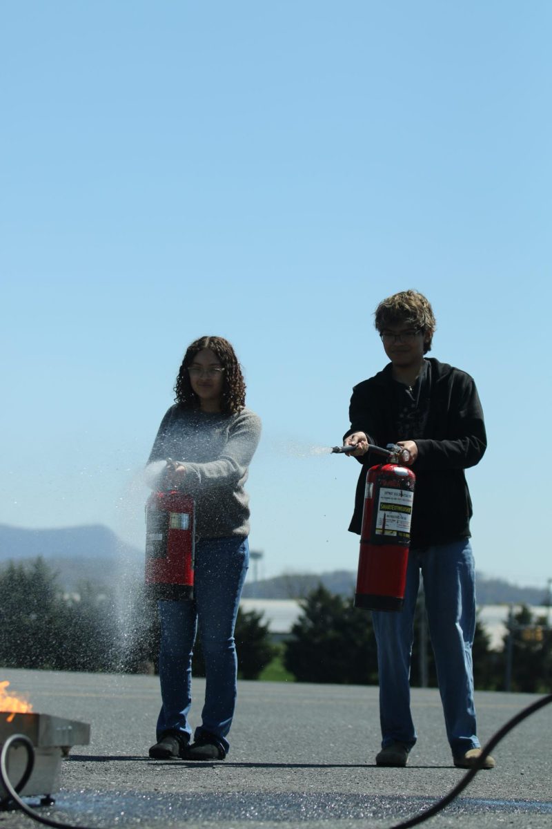 Freshman, Mariah Nelson and Senior, Joseph Geovanny using a fire extinguisher  