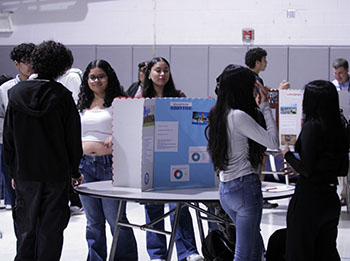 Eighth graders approach a board with their papers ready.