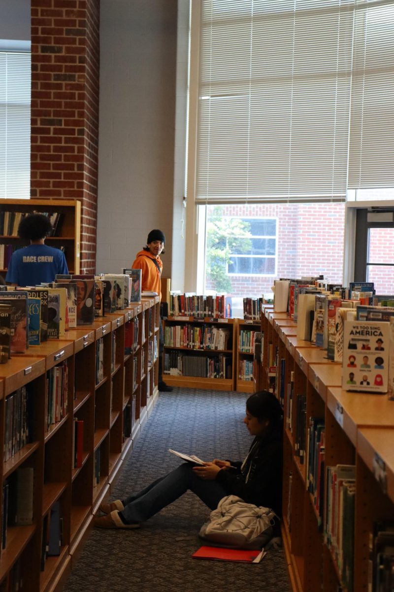 Student resting against the bookshelves reading a book. 